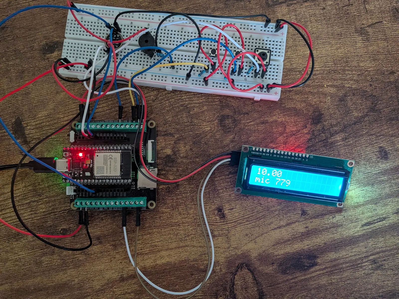 ESP32 timer prototype on a wooden desk, wired to a breadboard with a microphone, buzzer and three buttons, plus a 16×2 LCD
